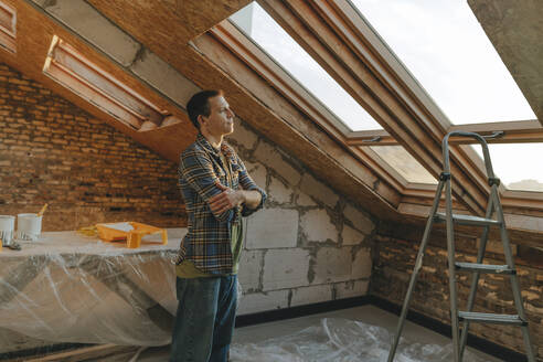 Thoughtful man standing with arms crossed and looking out of window at home - YTF01618