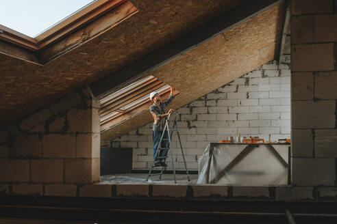 Construction worker standing on ladder and working in room under renovation - YTF01624