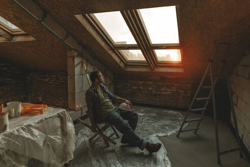 Bauarbeiter sitzt auf einem Tisch in der Nähe des Fensters in einem zu renovierenden Raum - YTF01626