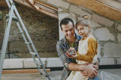 Daughter holding house model and sitting with father in attic - YTF01627
