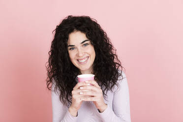 Glückliche Frau hält Einweg-Kaffeebecher gegen rosa Hintergrund - LMCF00799