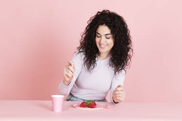 Glückliche junge Frau mit Erdbeeren und Kaffeetasse am Tisch - LMCF00801