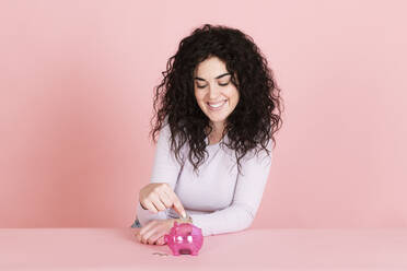 Glückliche Frau spart Geld in Sparschwein gegen rosa Hintergrund - LMCF00808