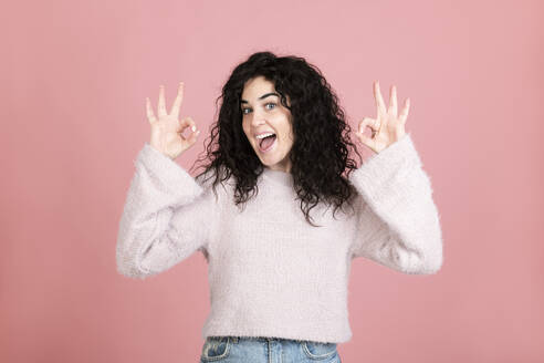 Cheerful young woman gesturing OK sign against pink background - LMCF00812