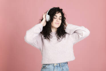 Frau mit drahtlosen Kopfhörern hört Musik vor rosa Hintergrund - LMCF00814