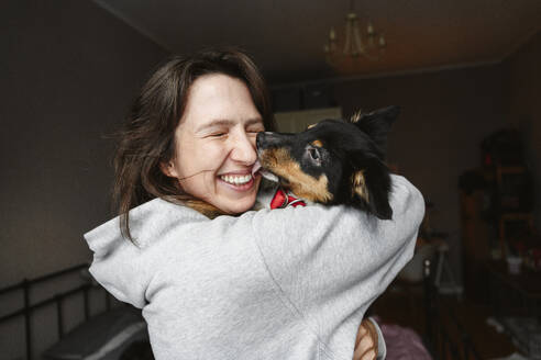 Happy woman with eyes closed holding dog at home - EYAF02926