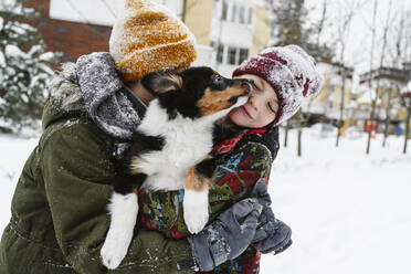 Playful siblings holding dog together in arms on snow - EYAF02937