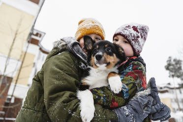 Brothers wearing warm clothes and holding dog in winter - EYAF02938