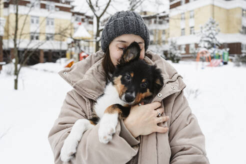 Woman covering dog with winter jacket on snow - EYAF02939