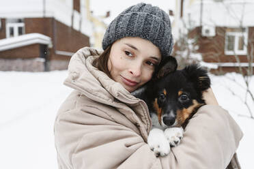 Frau trägt Strickmütze und umarmt Hund im Winter - EYAF02940