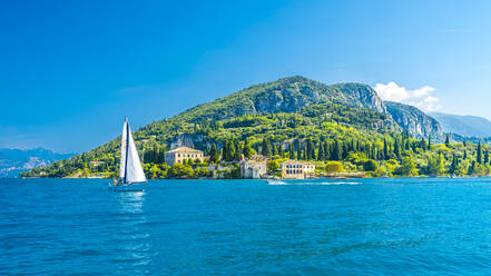 Italy, Veneto, Punta San Vigilio, Lake Garda in summer with mountain and single sailboat in background - MHF00749