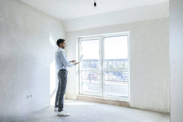 Architekt mit Laptop und am Fenster stehend auf der Baustelle - AAZF01389