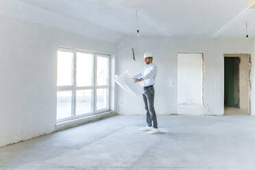 Architect examining blueprint at construction site - AAZF01394