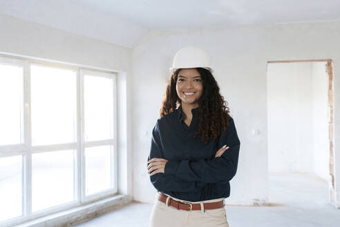 Smiling architect with arms crossed standing at construction site - AAZF01404