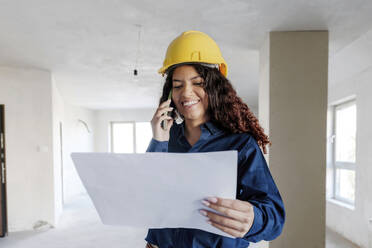 Happy young architect having discussion over blueprint on mobile phone at construction site - AAZF01426