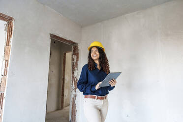 Lächelnder Architekt mit gelbem Schutzhelm und einem Tablet-PC auf der Baustelle - AAZF01429