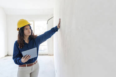 Architekt hält Tablet-PC und begutachtet Wand auf der Baustelle - AAZF01435