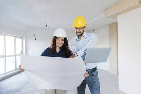 Happy architects discussing over blueprint at site - AAZF01438