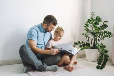 Father and daughter sitting on floor and reading book at home - OLRF00107