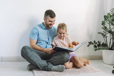Happy father and daughter reading book at home - OLRF00108