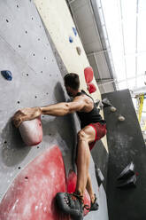 Athlete climbing on artificial wall in boulder gym - PBTF00397