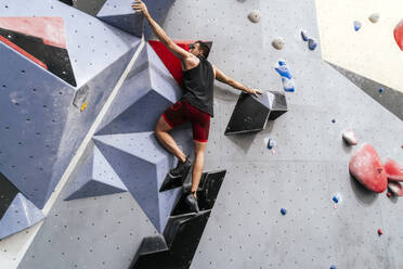 Athlete climbing on wall in boulder gym - PBTF00399
