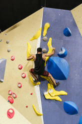 Sportler klettert an einer künstlichen Boulderwand in einer Sporthalle - PBTF00404