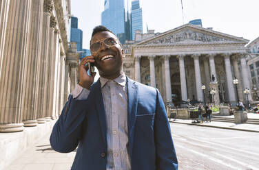 Smiling businessman talking on smart phone in London city - OIPF03774