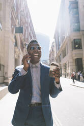 Happy businessman holding coffee cup and talking on mobile phone - OIPF03778