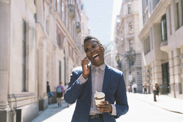 Fröhlicher Geschäftsmann, der eine Kaffeetasse hält und mit seinem Smartphone telefoniert - OIPF03779