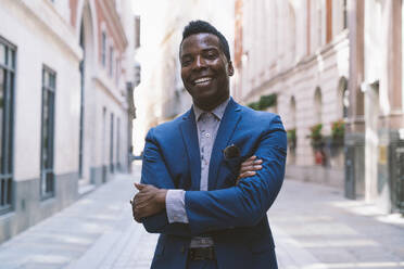 Smiling businessman standing with arms crossed on street - OIPF03780