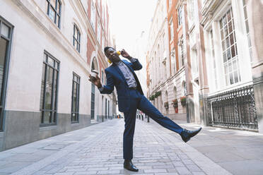 Happy businessman wearing wireless headphones and dancing on street - OIPF03788