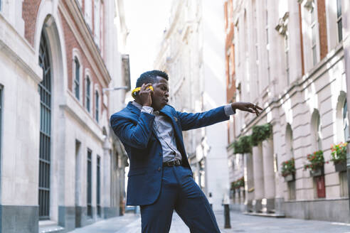 Businessman wearing wireless headphones and dancing on street - OIPF03790