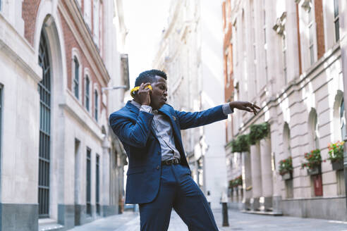 Geschäftsmann trägt drahtlose Kopfhörer und tanzt auf der Straße - OIPF03790