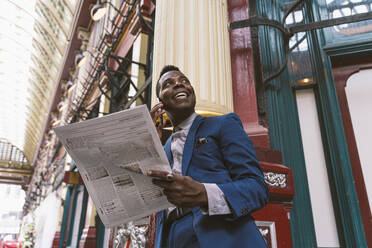 Happy mature businessman with newspaper talking on smart phone - OIPF03793