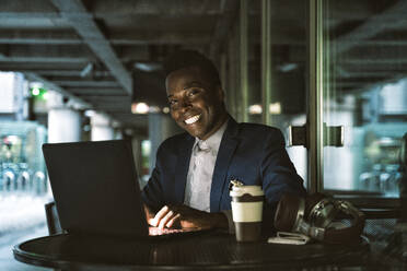 Smiling businessman working on laptop at cafe - OIPF03801