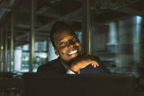 Happy businessman with hand on chin sitting in cafe - OIPF03806