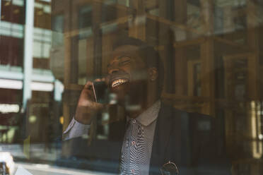 Glücklicher Geschäftsmann, der mit seinem Smartphone spricht, gesehen durch Glas - OIPF03809