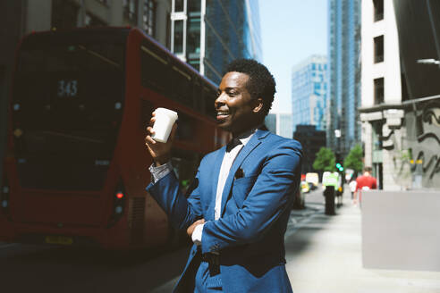 Smiling businessman standing with coffee cup on sunny day - OIPF03813