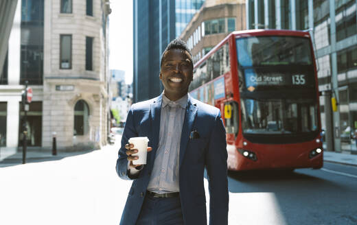 Happy businessman standing with coffee cup on sunny day - OIPF03814