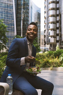 Lächelnder reifer Geschäftsmann sitzt mit einer Schüssel Salat im Büropark - OIPF03821