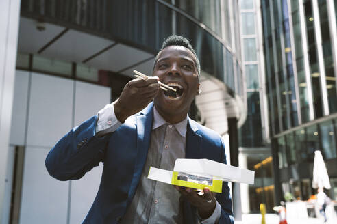 Happy mature businessman eating sushi in front of buildings - OIPF03833