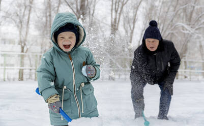 Fröhlicher Junge spielt mit Großvater im Schnee im Park - MBLF00246