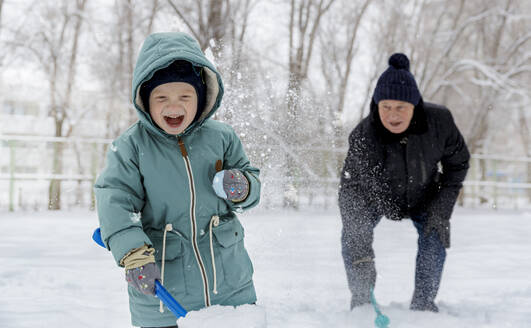 Cheerful boy playing with grandfather in snow at park - MBLF00246