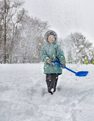 Fröhlicher Junge hält eine Schaufel in der Hand und spielt mit Schnee im Park - MBLF00248