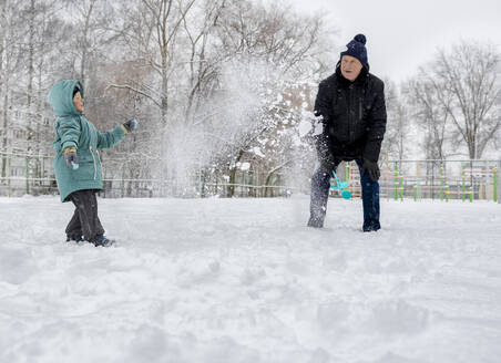 Glücklicher Junge spielt mit Großvater im Schnee im Park - MBLF00249