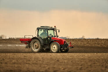 Landwirt im Traktor bei Sonnenuntergang, der das Feld für den Anbau vorbereitet - NOF00907