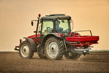 Landwirt im Traktor beim Sprühen von Dünger auf einem Feld bei Sonnenuntergang - NOF00910