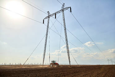 Traktor bei der Kultivierung eines Feldes in der Nähe eines Strommastes an einem sonnigen Tag - NOF00916