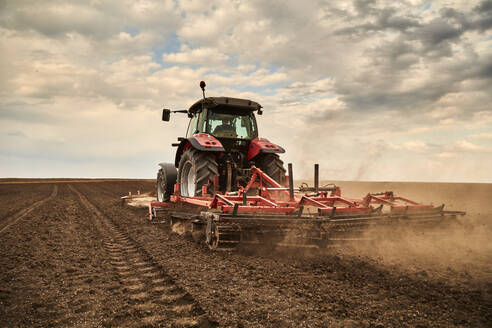 Landwirt im Traktor mit Pflug bei der Feldbestellung an einem bewölkten Tag - NOF00917